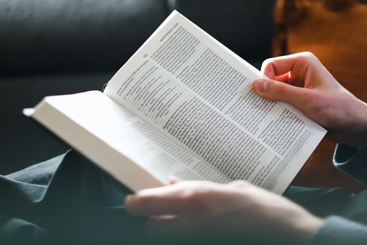 A person reads a book on a wooden table in warm daylight, representing the deep engagement of contextual language learning