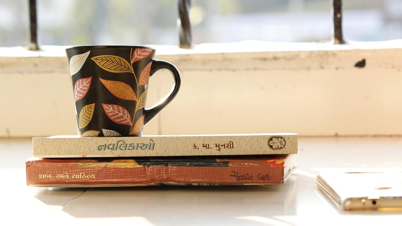 Stack of books beside a steaming coffee cup in a cozy reading setup for Spanish language learning